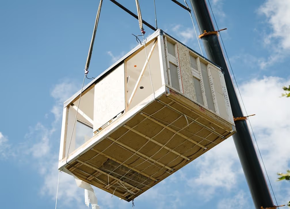 A factory-built module lifted by crane against a blue sky